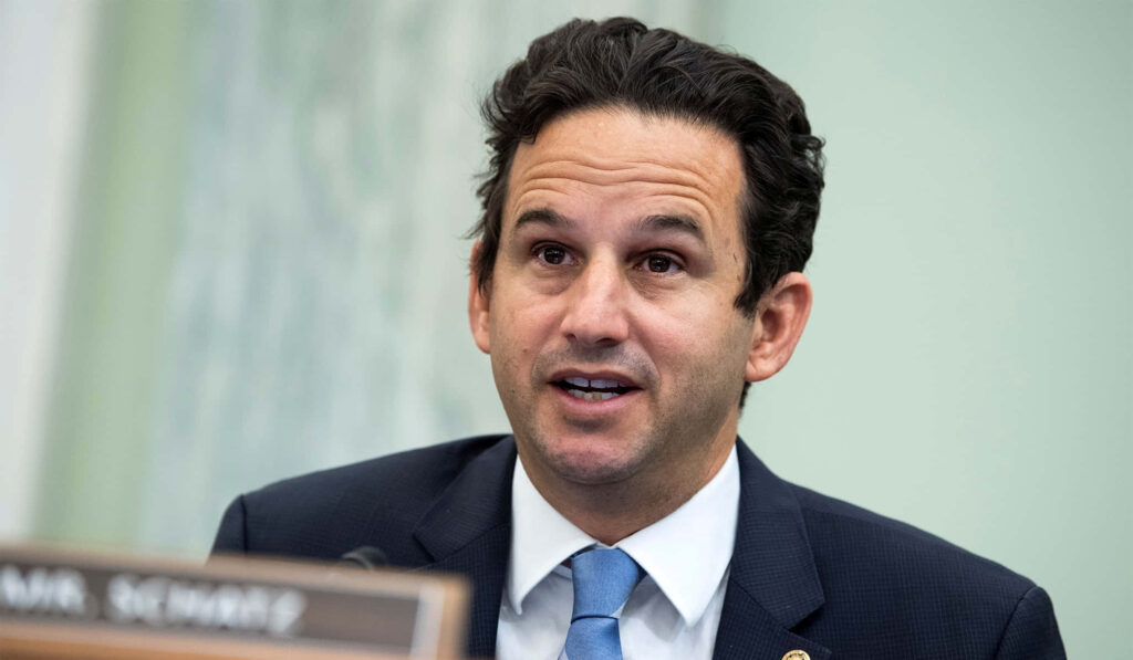 Senator Brian Schatz speaking at formal committee session with muted government backdrop Wallpaper