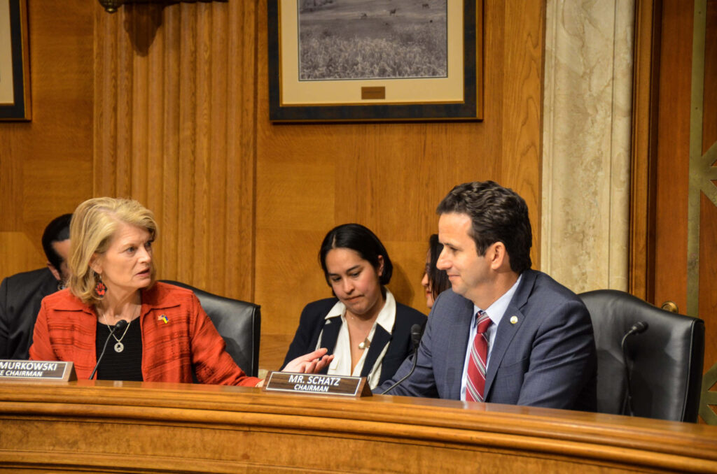 Senator Brian Schatz engaging in serious discussion with Senator Murkowski in committee room Wallpaper