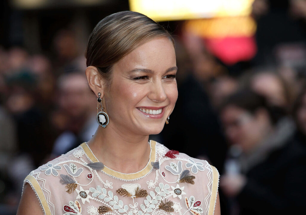 Brie Larson smiling in sheer floral dress with cameo earrings elegant portrait wallpaper background