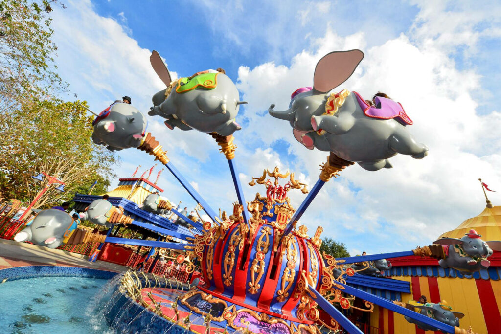 Dumbo ride vehicles fly over ornate Disneyworld carousel under bright blue sky with clouds Wallpaper