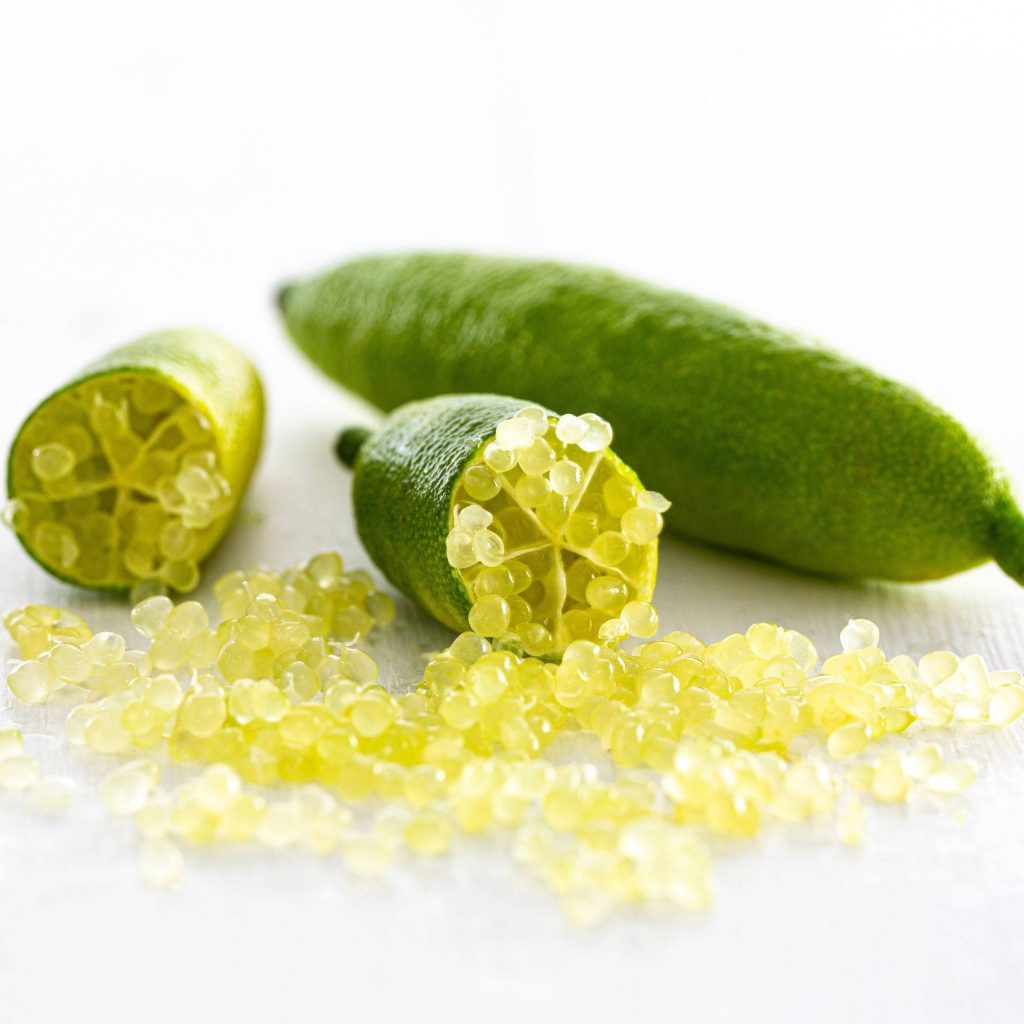 Macro photo of sliced green Australian finger limes showing caviar-like citrus vesicles on white Wallpaper