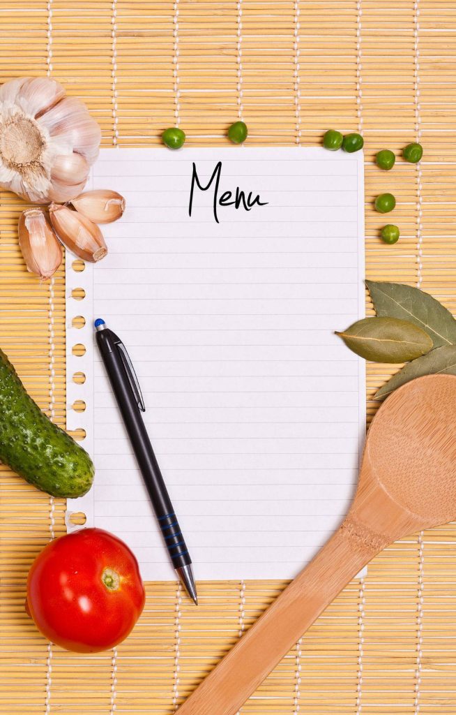 Flat lay of blank lined menu pad on bamboo mat with fresh garlic tomato cucumber peas bay leaves pen wooden spoon Wallpaper