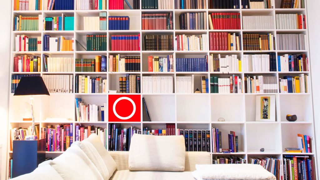 Bright virtual Zoom wallpaper with colorful books on white grid shelves and cozy couch