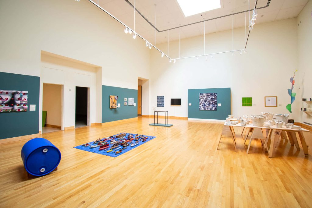 Bright airy art gallery Zoom background with hardwood floors blue boat display and ceramic art Wallpaper