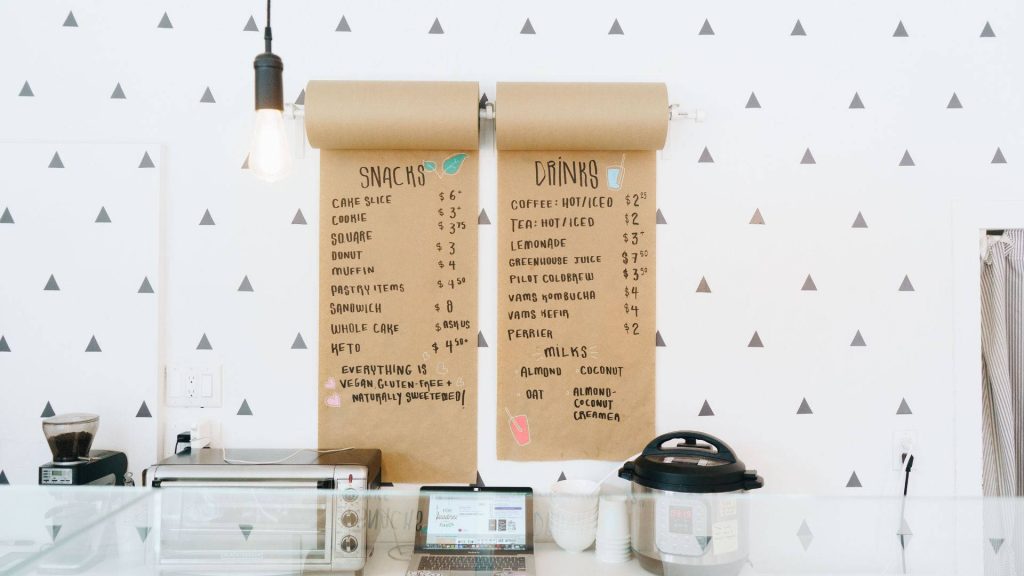 Minimalist cafe menu on rustic brown butcher paper with vegan gluten-free snacks on white wall Wallpaper