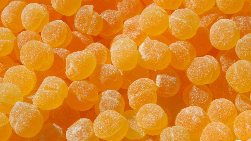 Close-up of glossy orange sugar candies coated in sparkling crystals vibrant candy wallpaper background