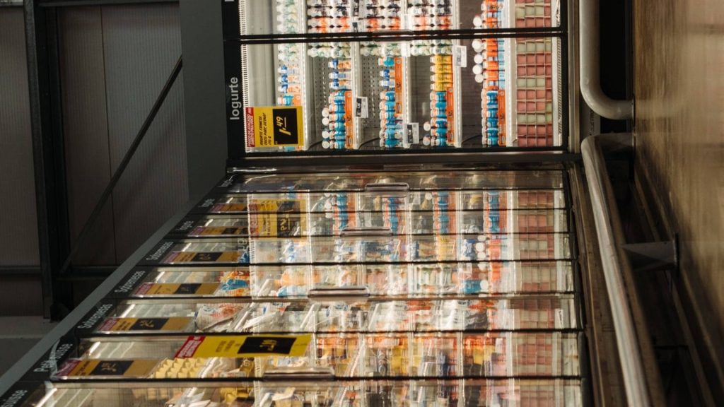 Bright organized grocery store dairy aisle with glass door refrigerators stocked with yogurt products Wallpaper