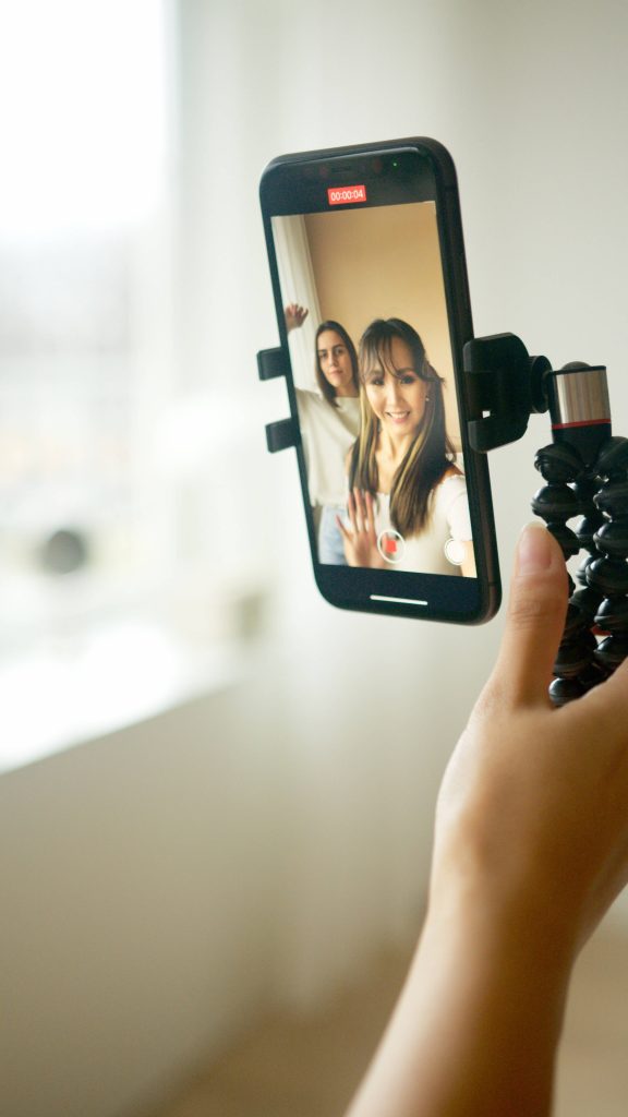 POV smartphone on flexible tripod recording two women vlogging in bright natural indoor light Wallpaper