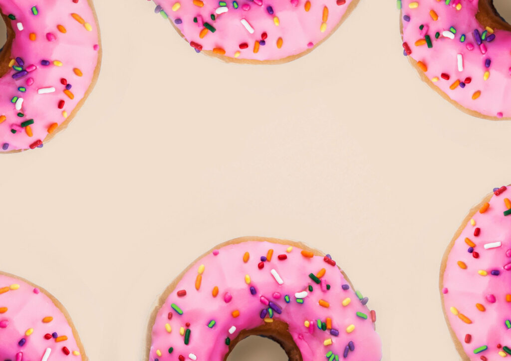 Donut wallpaper with pink icing and colorful sprinkles on beige background dessert pattern