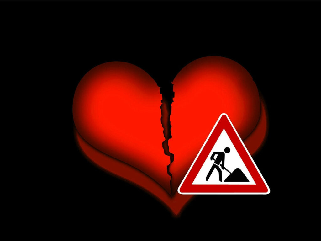 Bright red broken heart with maintenance sign on black background symbolizing healing recovery Wallpaper