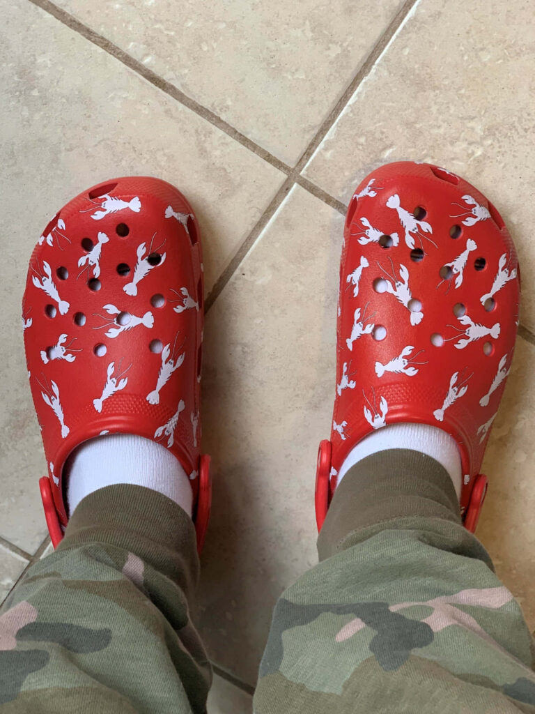 Red Crocs with white crawfish pattern worn with white socks and camo pants on tiled floor Wallpaper