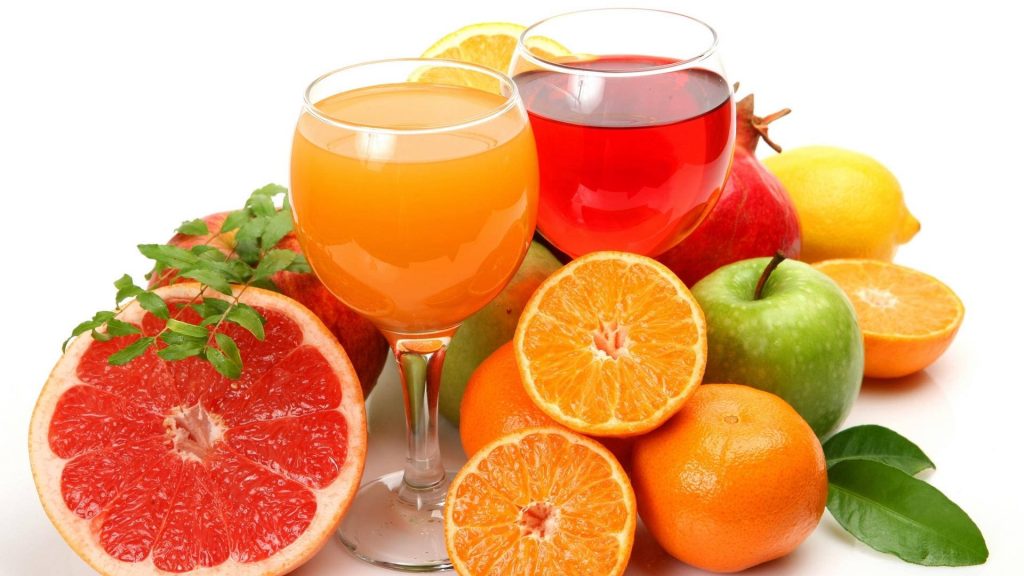 Two glasses of fresh fruit juice with grapefruit oranges apple lemon pomegranate on white background Wallpaper