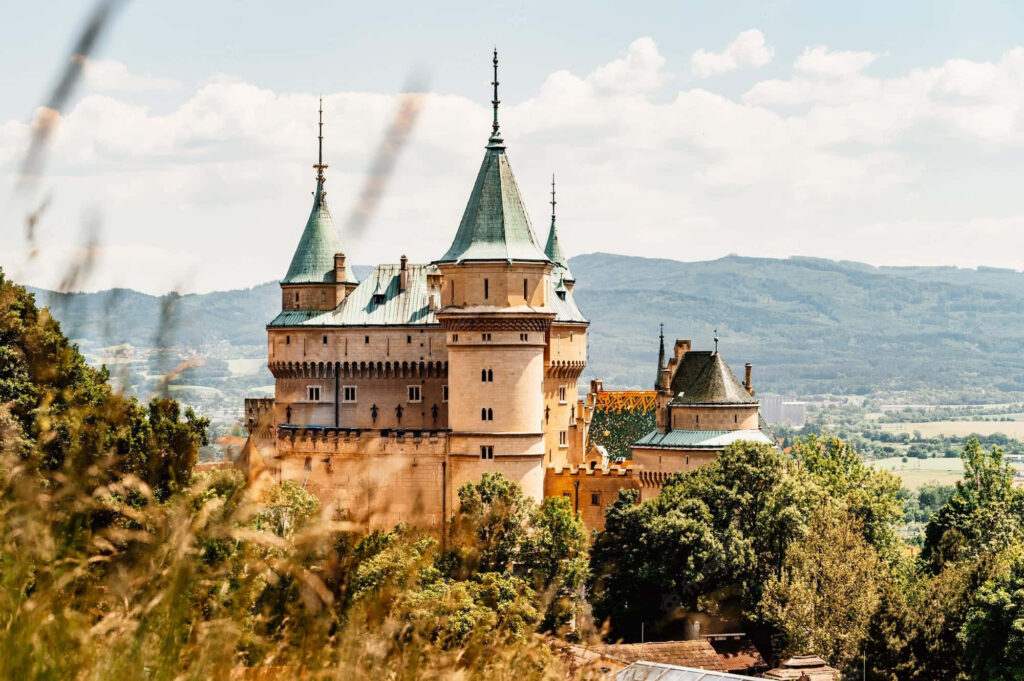 Bojnice Castle in Slovakia with medieval turrets lush greenery and clear blue sky background Wallpaper