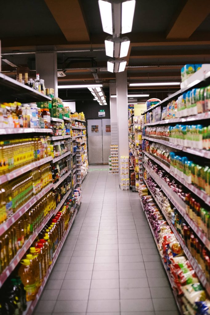 Bright supermarket aisle with stocked shelves tiled floor and industrial lighting wallpaper background