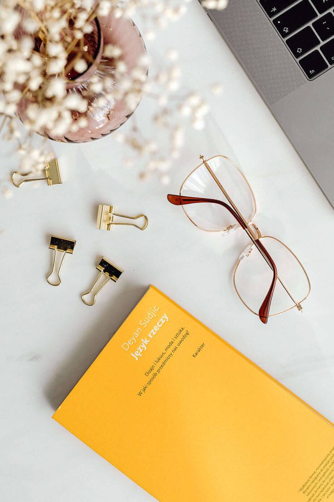 Bright yellow Deyan Sudjic book flat lay with marble desk laptop glasses floral vase workspace Wallpaper