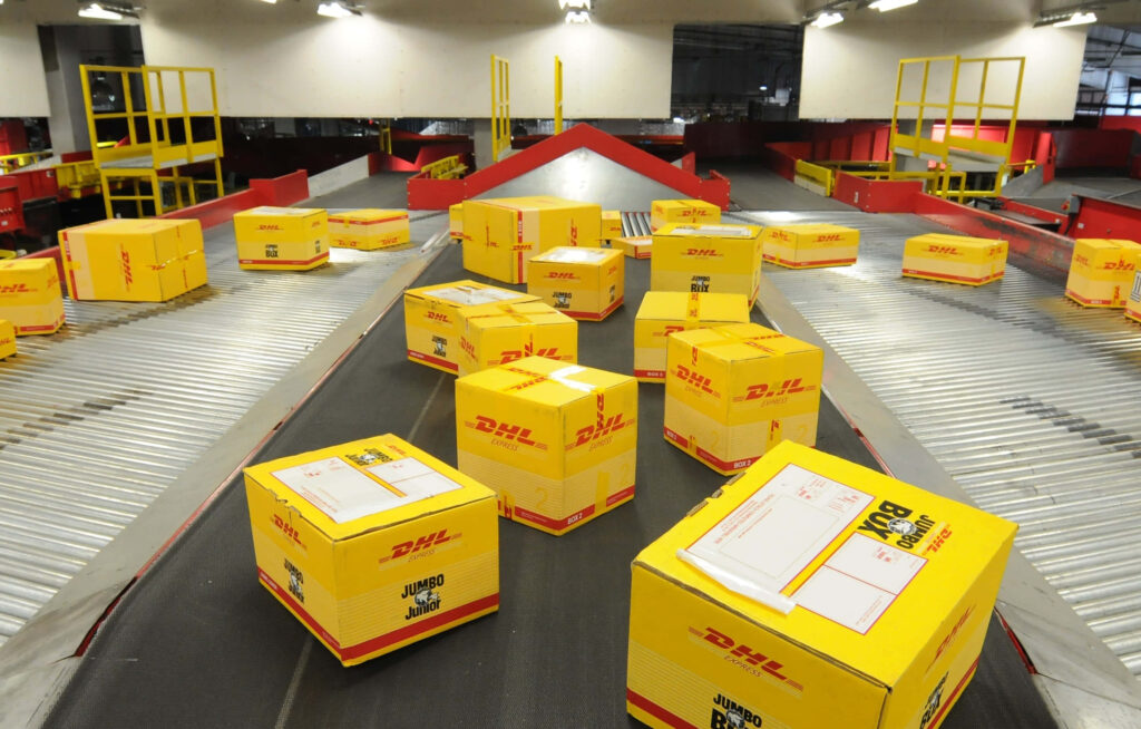Bright yellow DHL boxes on conveyor belt in high-tech warehouse showcasing efficient logistics Wallpaper