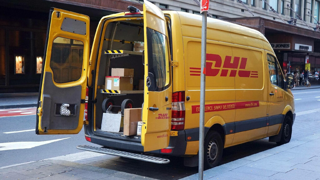 Bright yellow DHL delivery van with open rear doors full of packages in busy city street Wallpaper