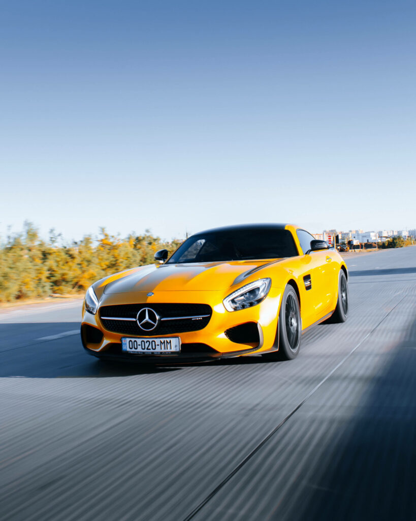 Bright yellow Mercedes AMG GT R speeding on open road with clear blue sky background wallpaper