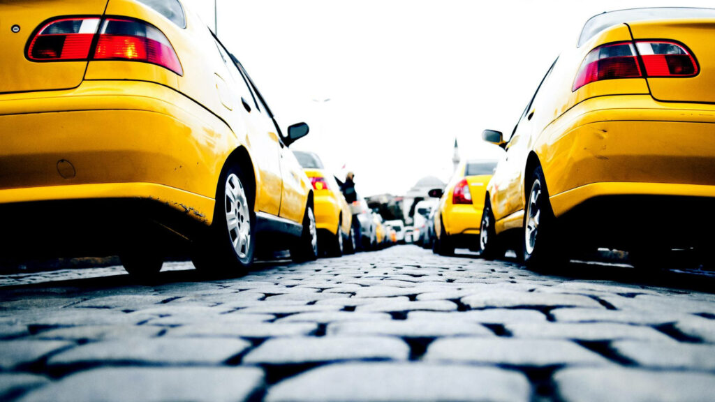 Low-angle view of bright yellow taxis lined on cobblestone street vibrant urban city scene wallpaper