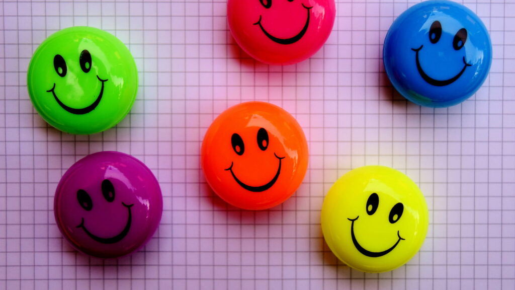 HD wallpaper with five glossy neon smiley badges on a clean graph paper background vibrant colors