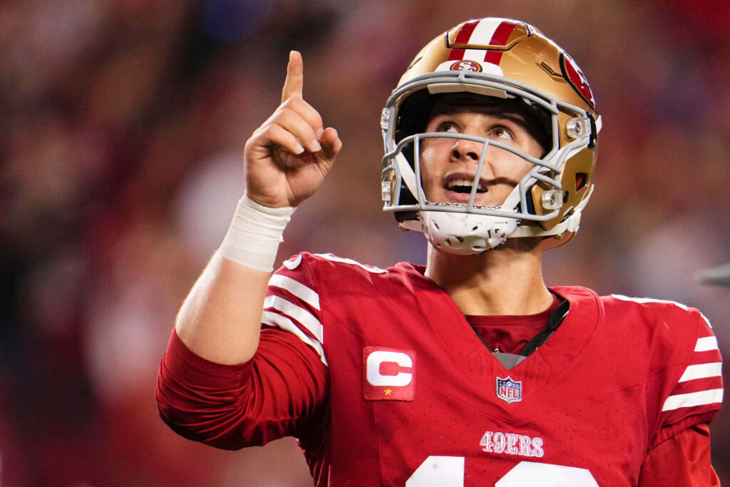 Brock Purdy 49ers quarterback in red uniform points up in vibrant stadium showing leadership Wallpaper