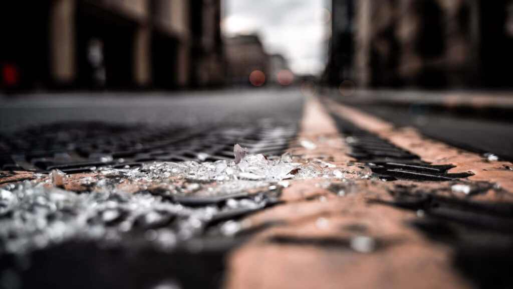 Broken glass scattered on urban pavement reflecting light creating edgy textured street scene background Wallpaper