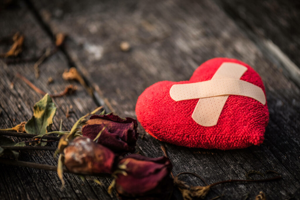 Plush red heart with bandage and withered roses on wood background symbolizing heartbreak Wallpaper