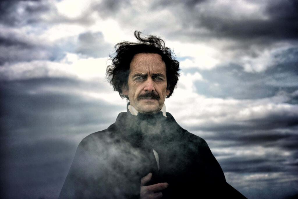 Brooding Edgar Allan Poe impersonator under stormy sky with mist evokes gothic mystery wallpaper