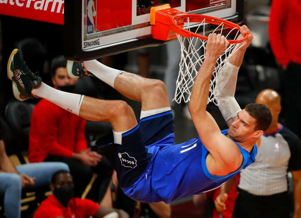 Brook Lopez hanging on basketball rim in blue jersey mid dunk NBA action wallpaper background
