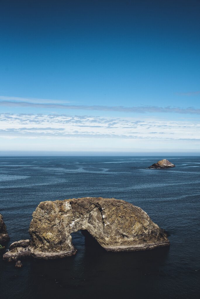 Rugged Brookings coastal rocks meet deep blue ocean under dramatic cloudy sky wallpaper background