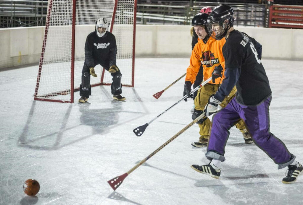 Exciting Broomball Action on Ice: Players in Orange, Black, Purple Jerseys Wallpaper