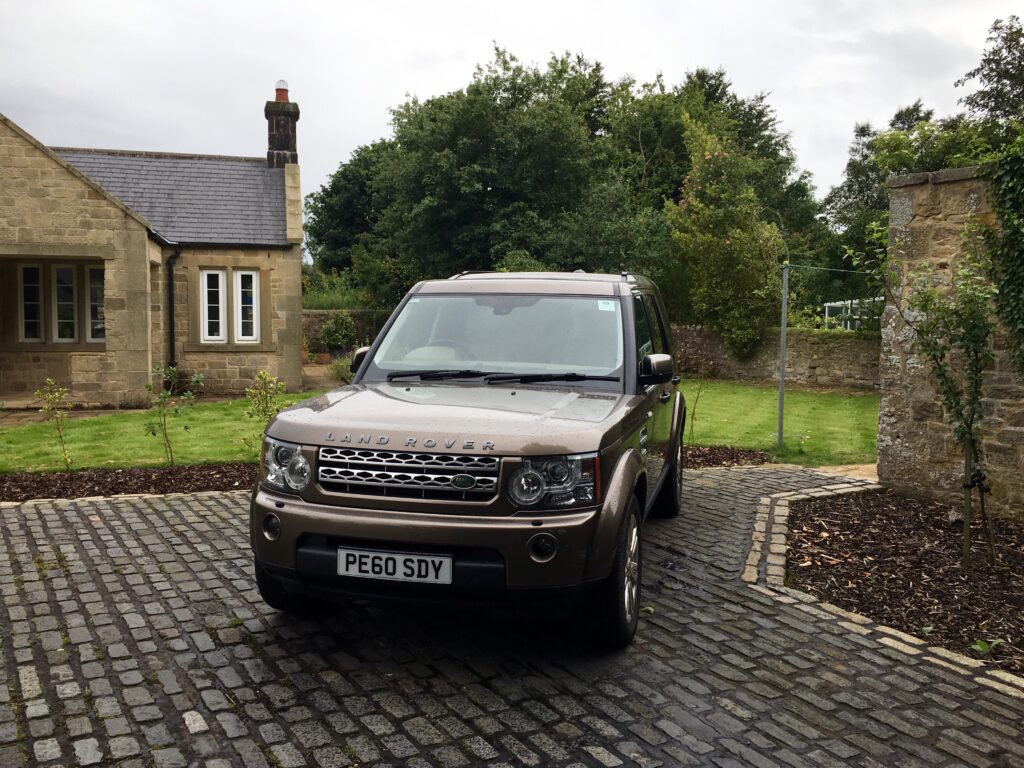 Brown Land Rover SUV on Cobblestone Driveway in Scenic Greenery Wallpaper