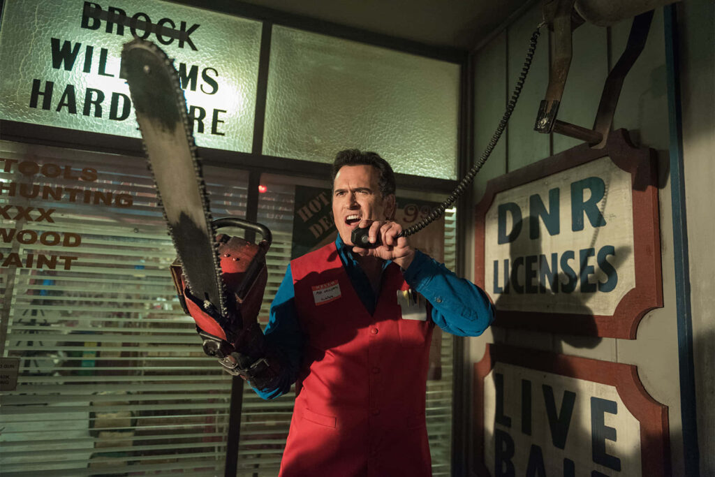 Bruce Campbell with chainsaw in red vest inside retro hardware store horror comedy wallpaper background
