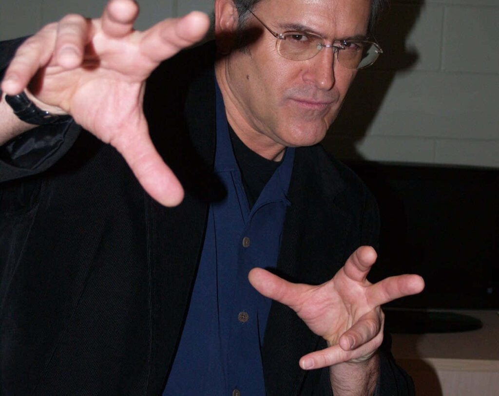 Bruce Campbell dynamic pose wearing glasses and dark jacket indoor neutral background wallpaper
