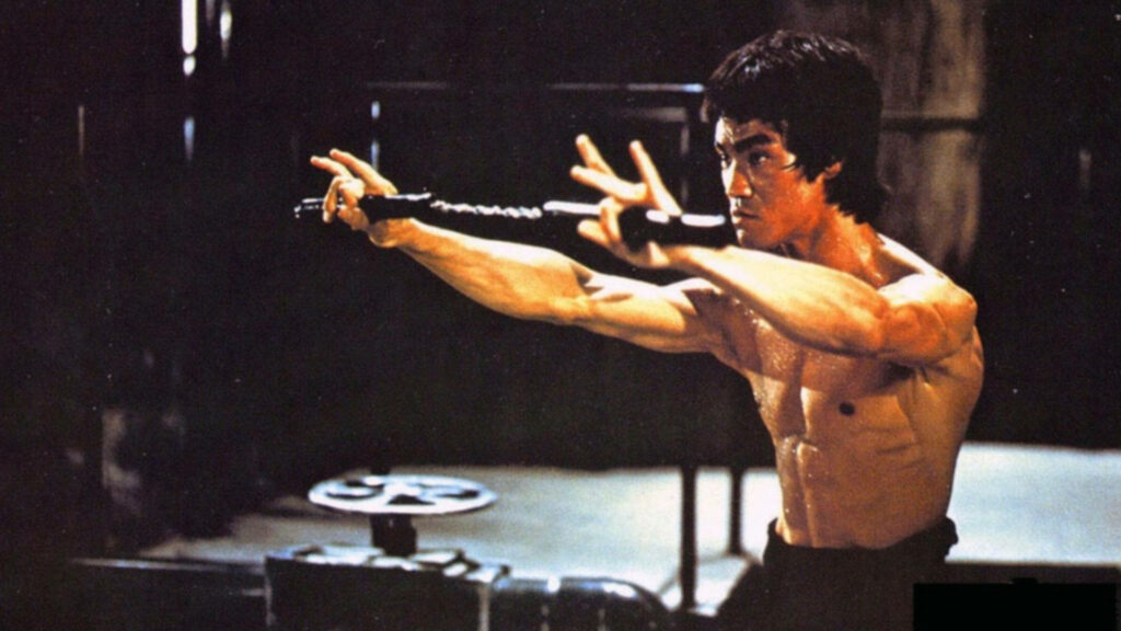 Bruce Lee shirtless in action pose wielding nunchaku gritty cinematic martial arts wallpaper