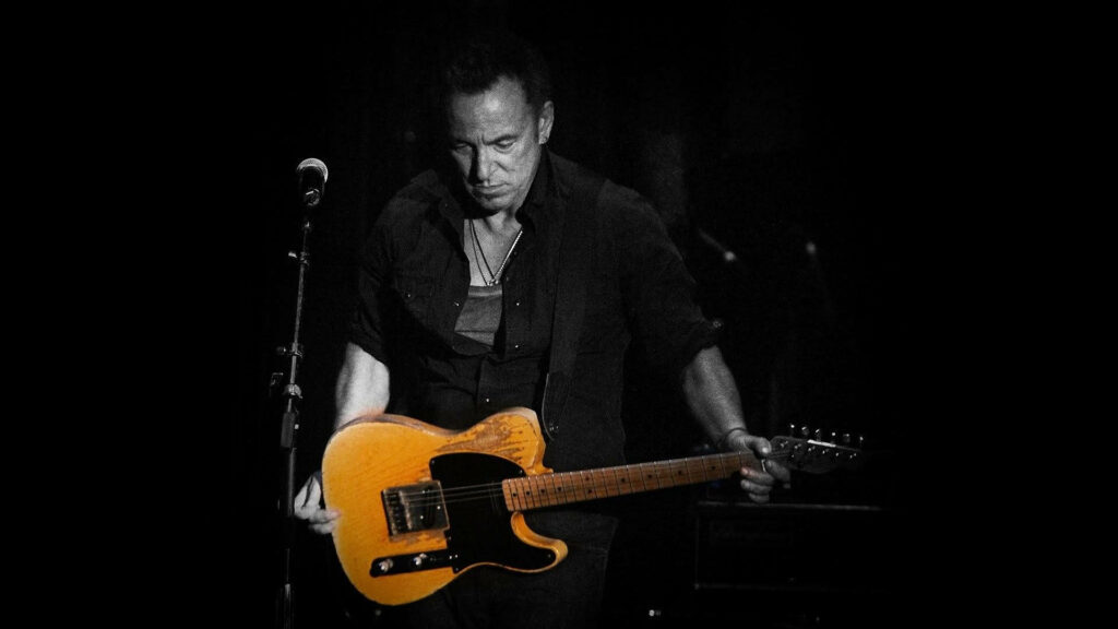 Bruce Springsteen playing Fender Telecaster guitar on stage with dramatic yellow lighting background Wallpaper