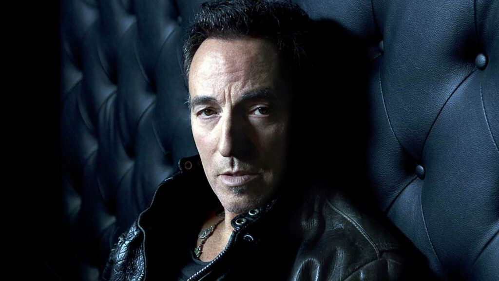Bruce Springsteen close-up portrait on black leather couch with moody blue tones classic rock wallpaper