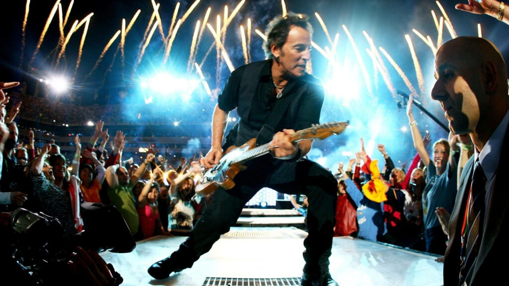 Bruce Springsteen performing live with guitar vibrant crowd fireworks dynamic rock concert wallpaper