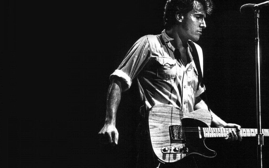 Bruce Springsteen playing guitar on stage at county fair with dramatic lighting and black background Wallpaper