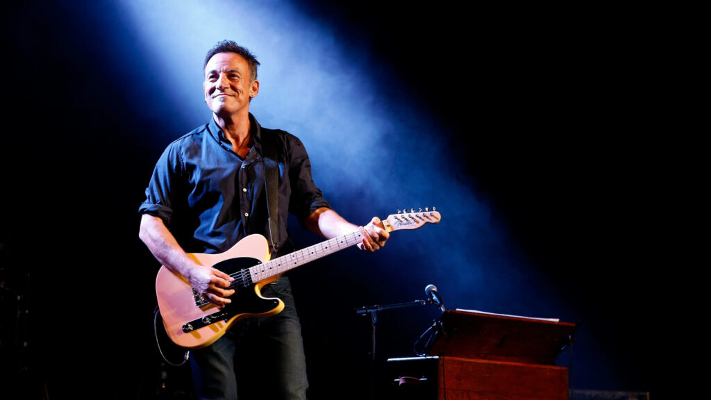 Bruce Springsteen performing live on stage with electric guitar under blue white lights wallpaper