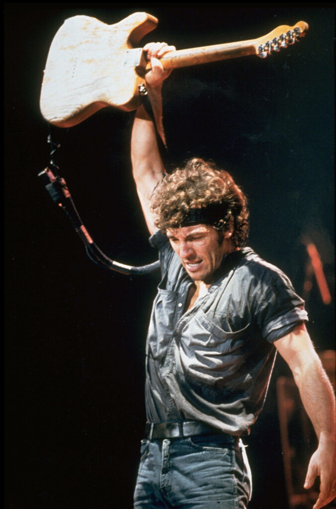 Bruce Springsteen live rock concert energetic pose leather outfit electric guitar vibrant lighting Wallpaper