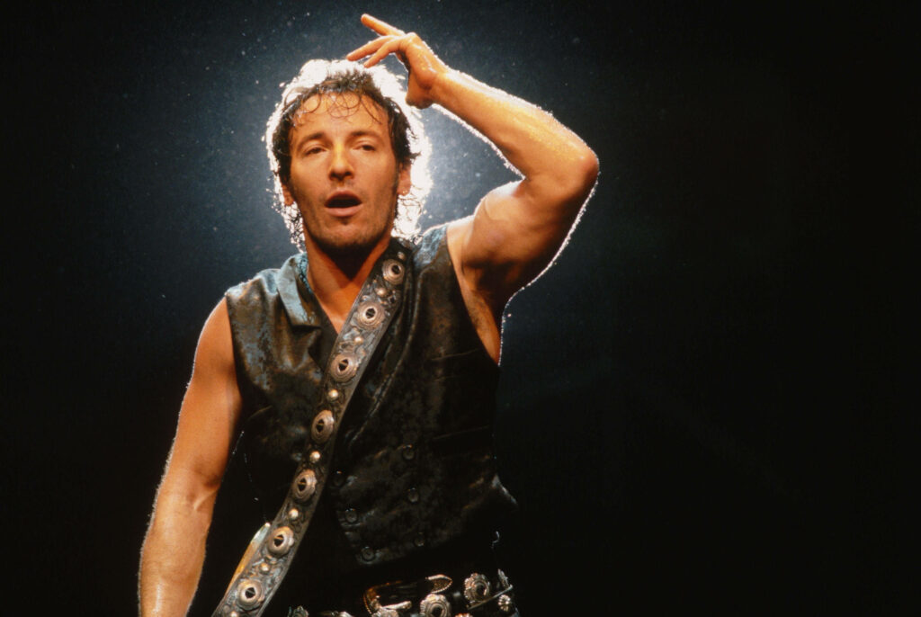 Bruce Springsteen performing live at Wembley Stadium 1980s rock concert vibrant stage lighting Wallpaper