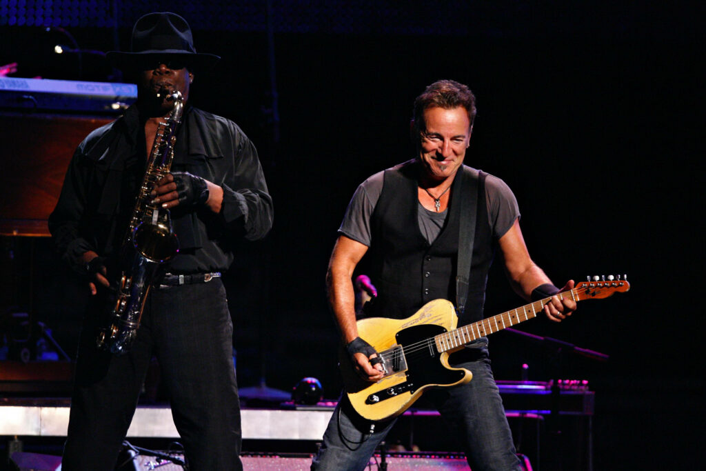 Bruce Springsteen electric guitar and Clarence Clemons saxophone live concert vibrant stage lighting Wallpaper