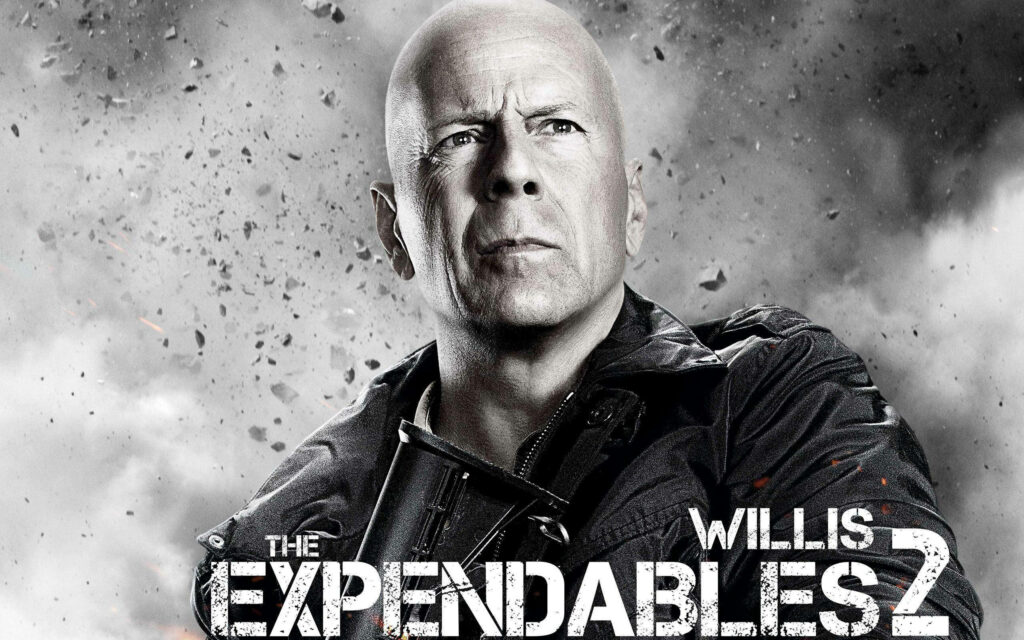 Bruce Willis in intense action pose with flying debris background Expendables 2 wallpaper