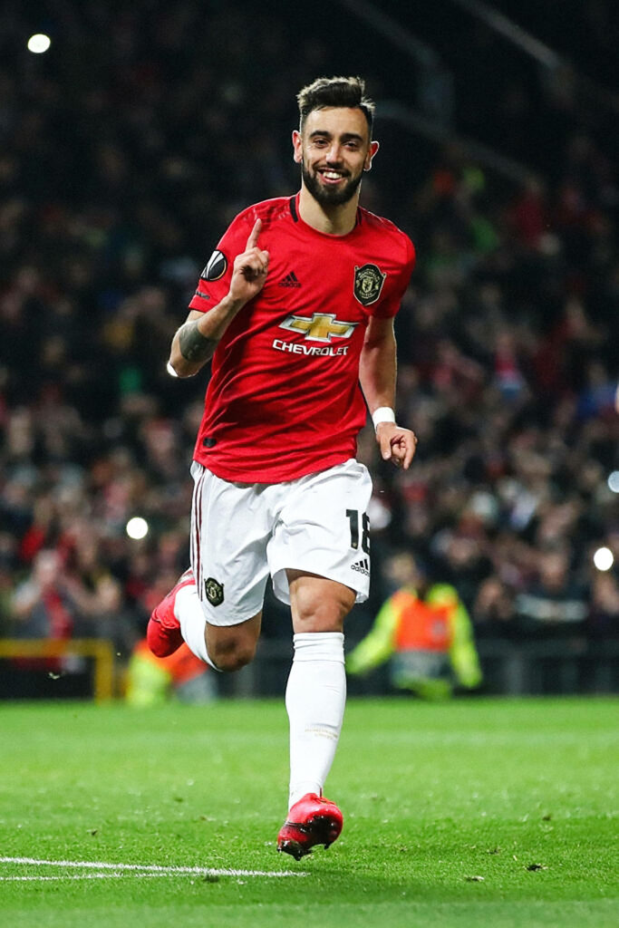 Bruno Fernandes Manchester United celebrating goal red kit dynamic pose vibrant stadium background Wallpaper