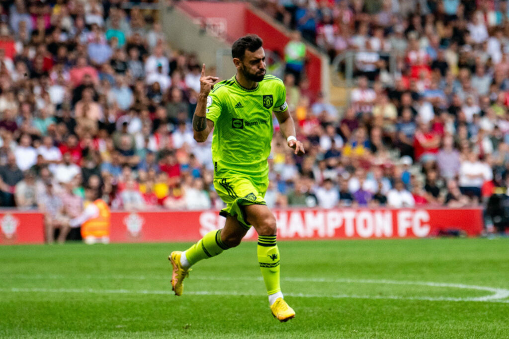 Bruno Fernandes in neon green Manchester United kit mid-action football field vibrant crowd wallpaper