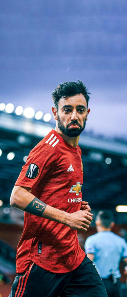 Bruno Fernandes Manchester United midfielder in red kit on pitch with stadium lights background Wallpaper
