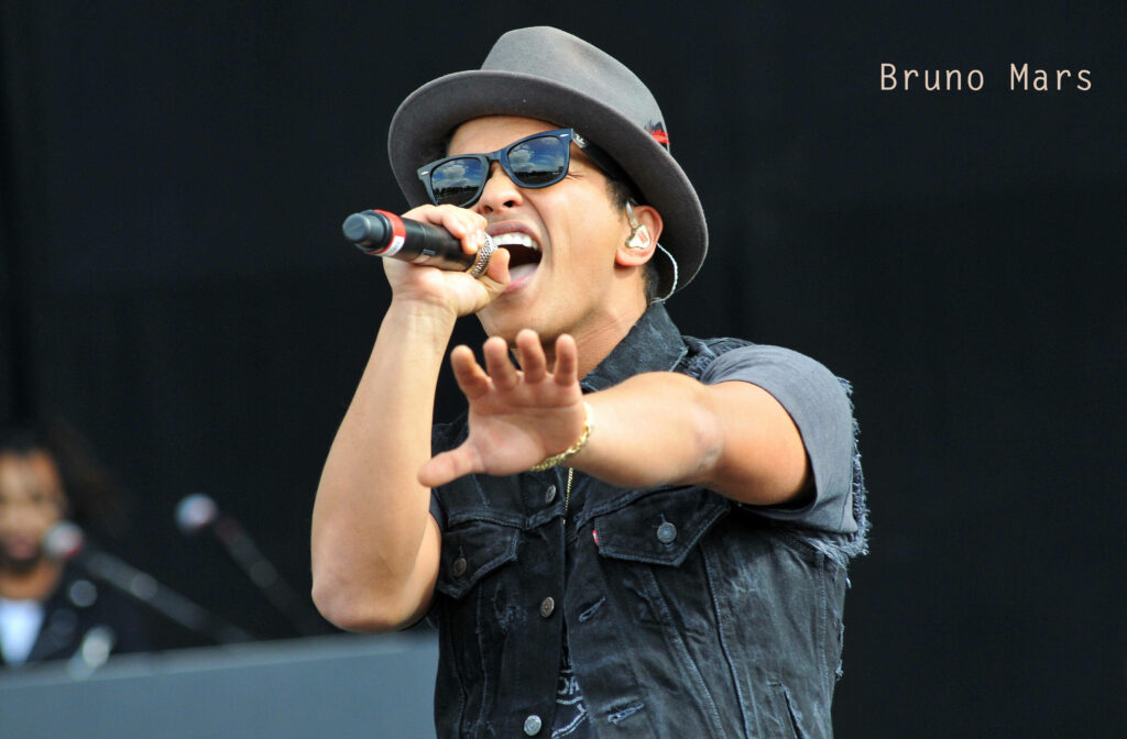 Bruno Mars singing passionately on stage in denim vest and stylish hat concert backdrop wallpaper