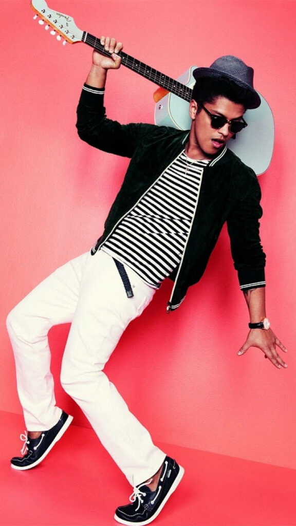 Bruno Mars smiling with guitar against vibrant pink background in retro striped shirt and sunglasses Wallpaper