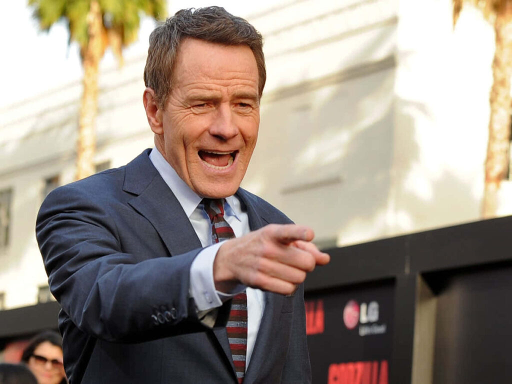 Bryan Cranston in sharp suit and striped tie smiling at outdoor event with palm trees backdrop Wallpaper